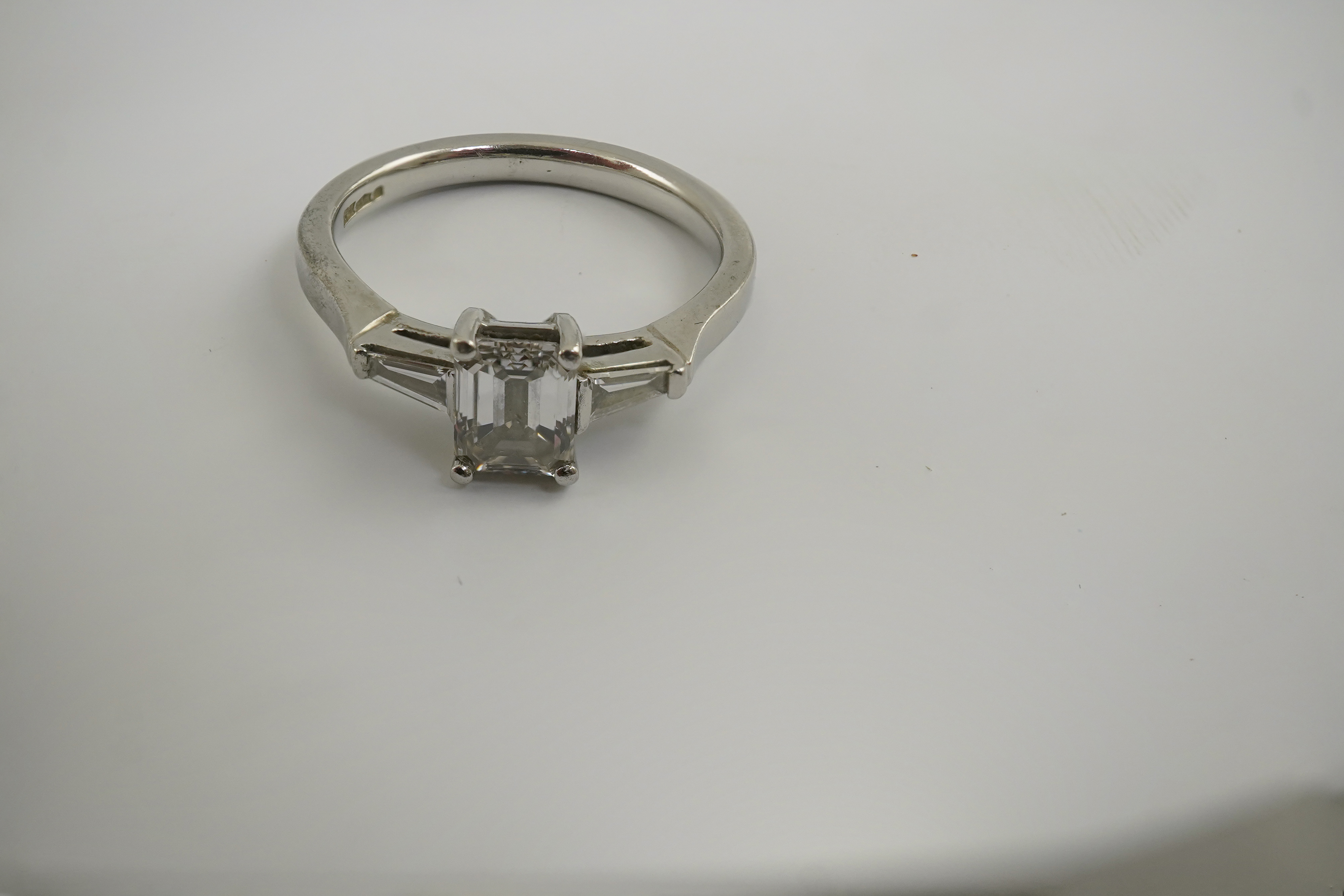 A modern platinum and single stone emerald cut diamond set ring, with two stone tapered baguette cut diamond set shoulders